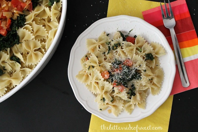 Spinach Tomato Bow Tie Pasta on a white plate with a fork.