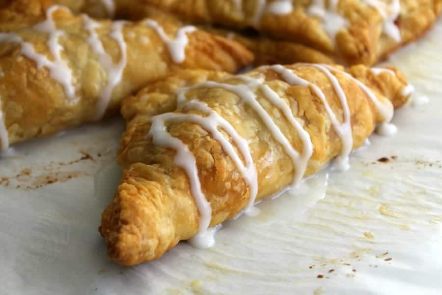 Pumpkin Pie Turnovers on parchment paper with icing drizzled over the top