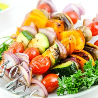 Grilled Vegetable Skewers on white plate with parsley and bowl of olive oil in background
