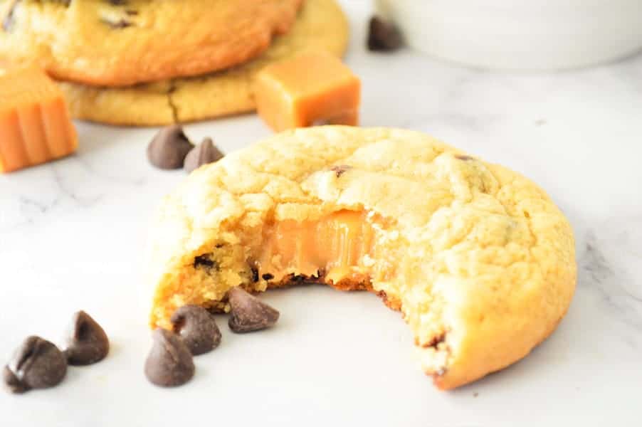 Ooey-gooey Chocolate Chip Caramel Cookies! Using a basic cookie recipe with a caramel stuffed inside for a delicious cookie! Chocolate Chip Caramel Cookies with bite and caramel oozing out