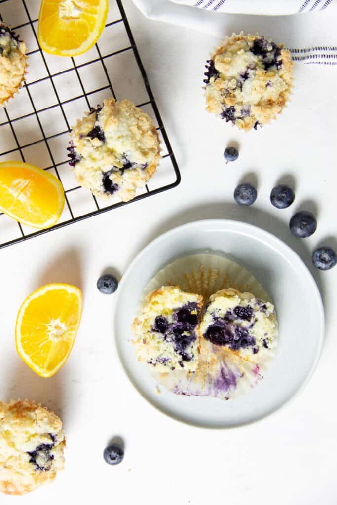 The best Orange Blueberry Muffins! So tender and moist, with a buttery crumb topping! Made with fresh blueberries and oranges! muffin cut in half on plate.