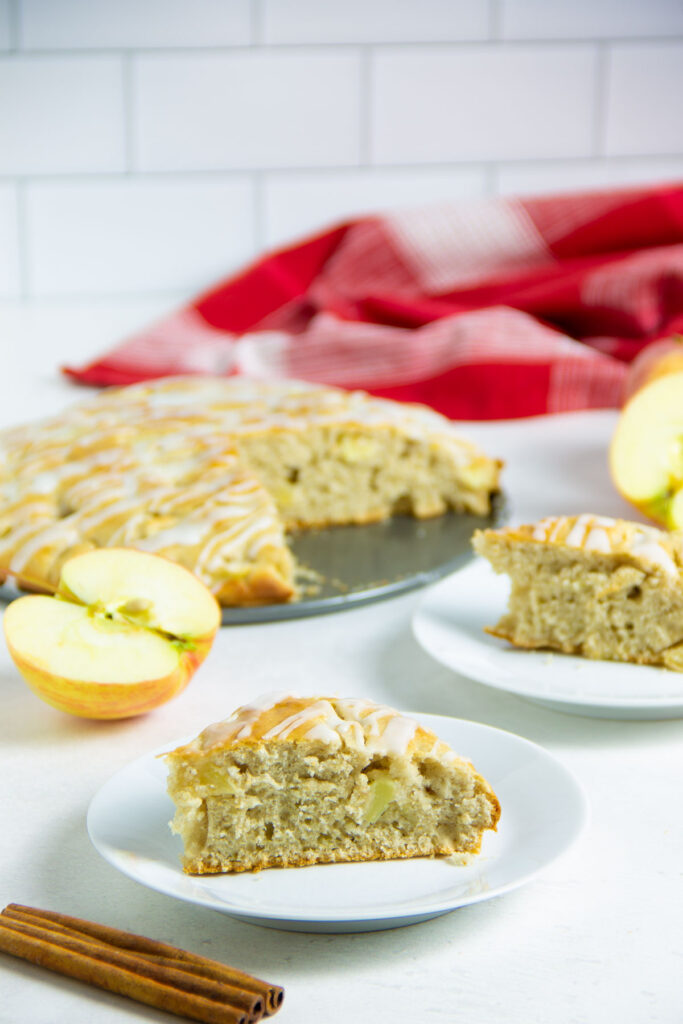 Easy Apple Cake! Made with just a few pantry staples and fresh apples! With a hint of cinnamon, this tasty dessert will become a favorite! apple cake on white plate with fresh cinnamon in front.