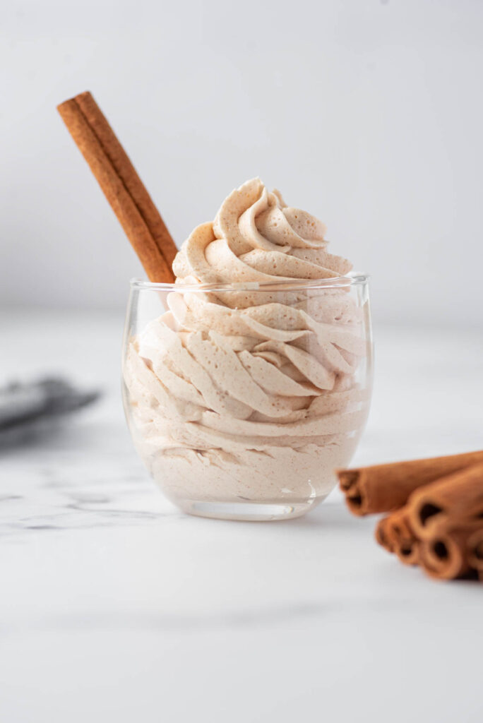A fast, simple Cinnamon Buttercream Frosting! Light and fluffy frosting that goes well on cake, cupcakes, and cookies! Cinnamon Buttercream Frosting piped into a glass with cinnamon stick.