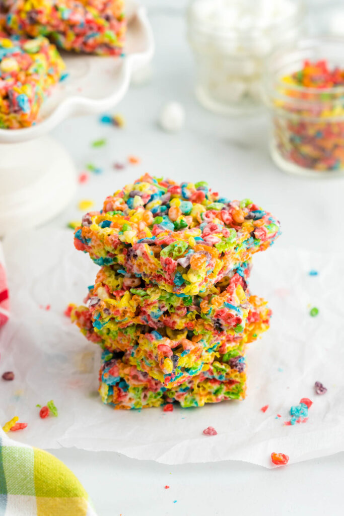 These Fruity Pebble Rice Krispie Treats are a fun and easy snack that even the kids can make! Just takes about 20 minutes! Fruity Pebbles Rice Krispie Treats stacked on parchment paper.