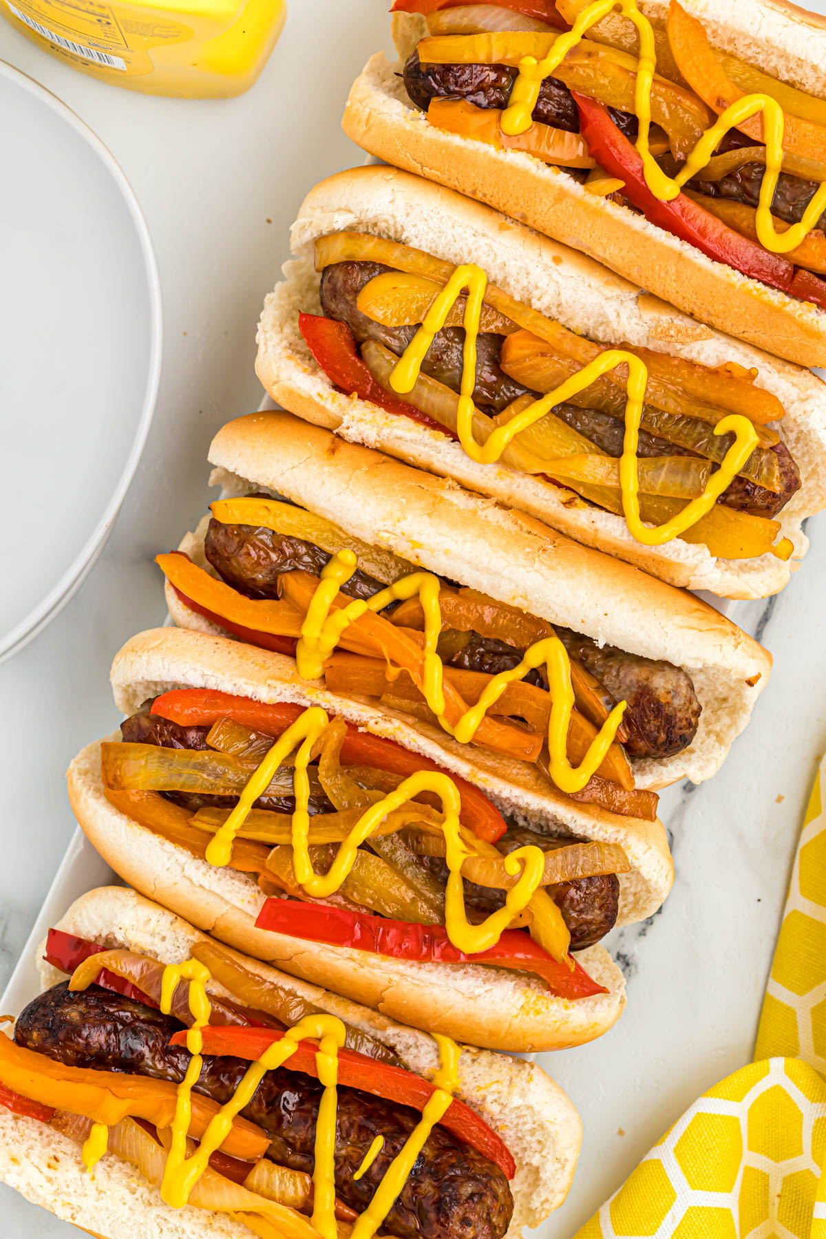 Quick and easy Air Fryer Bratwurst. Loaded with bell peppers and onions in a warm bun, topped with yellow mustard bratwurst in buns topped with peppers, onions, and mustard.