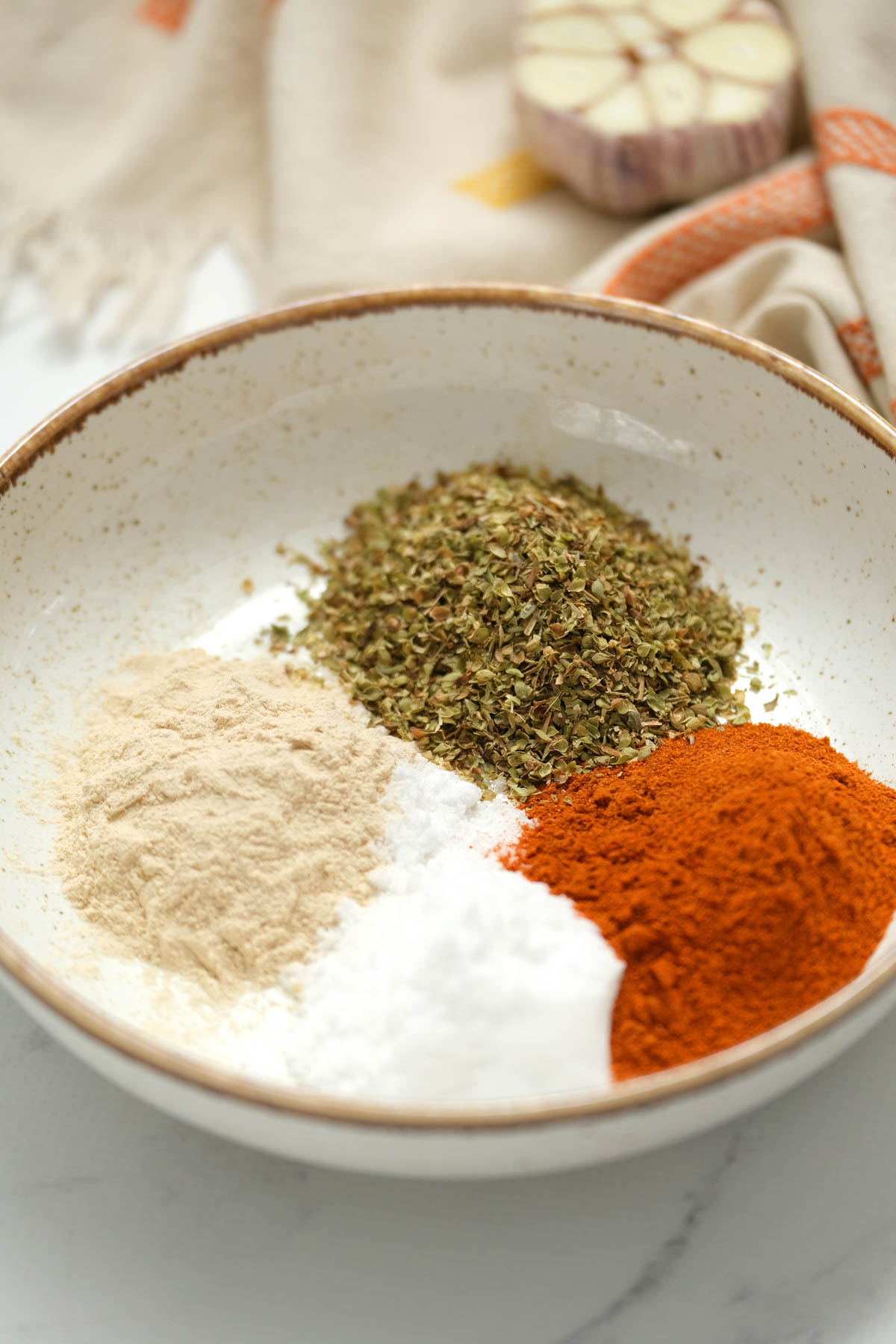 Spice up your meals with our all purpose seasoning blend recipe! Make mealtime more flavorful when cooking up pork, chicken, or veggies! A close-up photo of a bowl filled with all purpose seasoning blend, made with a variety of herbs and spices.