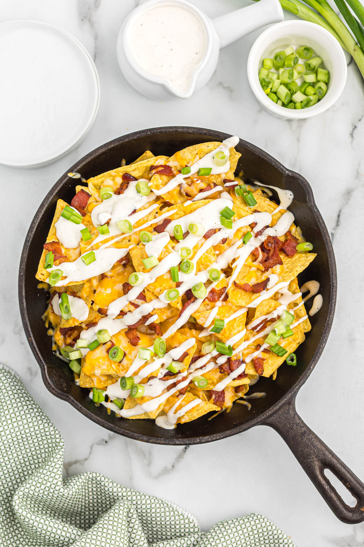 Whip up this quick and easy Bacon Ranch Skillet Nachos recipe in minutes. Crispy tortilla chips smothered in melty cheese, savory bacon, and creamy ranch dressing. overhead view of bacon ranch skillet nachos in skillet