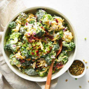 easy broccoli salad in white bowl with wooden spoon.