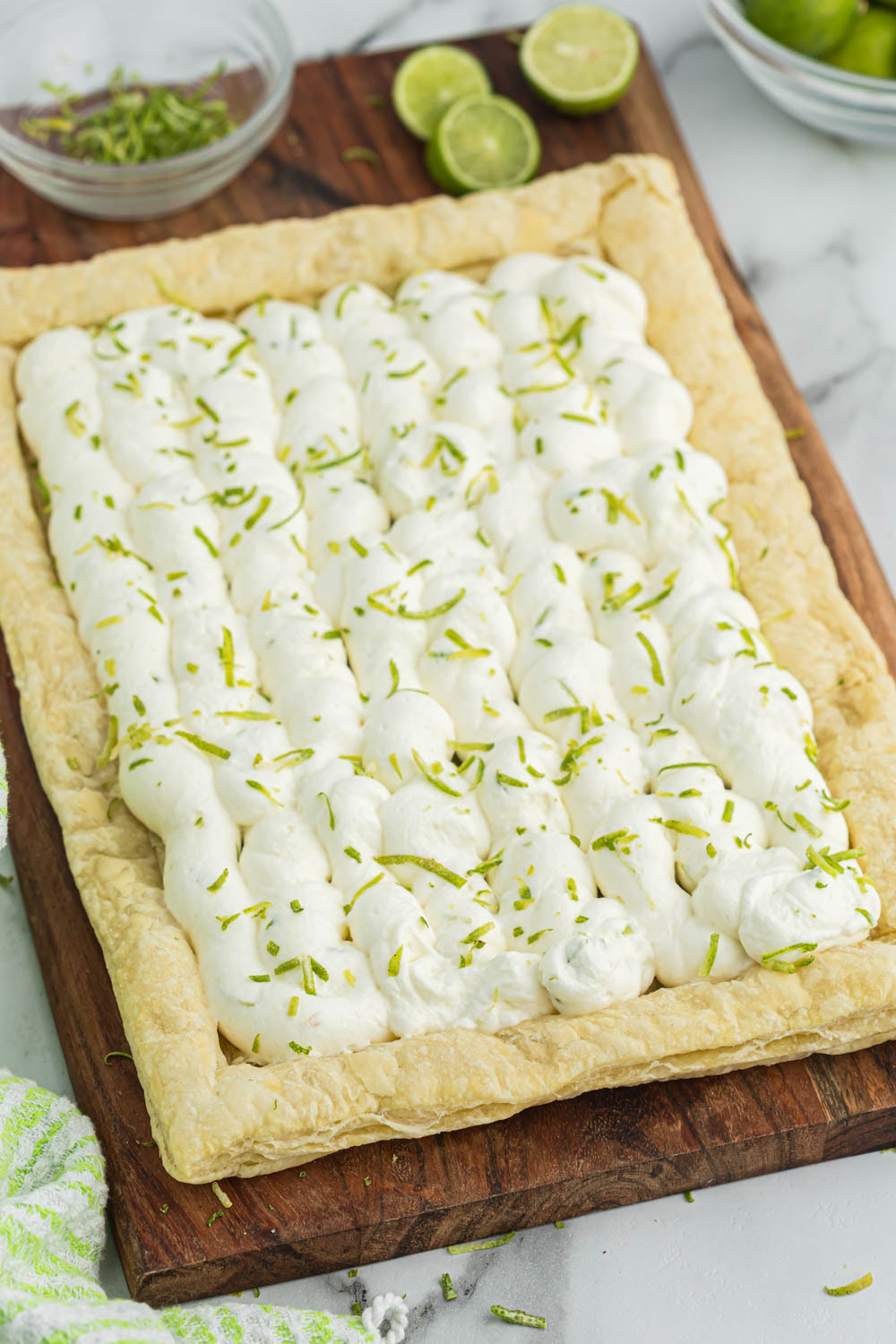 Key lime tart on wooden board with limes and zest.