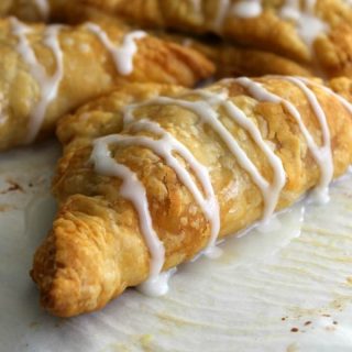 Pumpkin Pie Turnovers on parchment paper with icing drizzled over the top