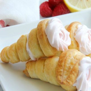 Lemon Raspberry Cream Horns stacked on white plate with raspberries and lemon