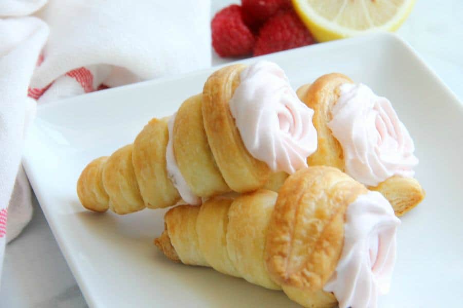 Lemon Raspberry Cream Horns stacked on white plate with raspberries and lemon