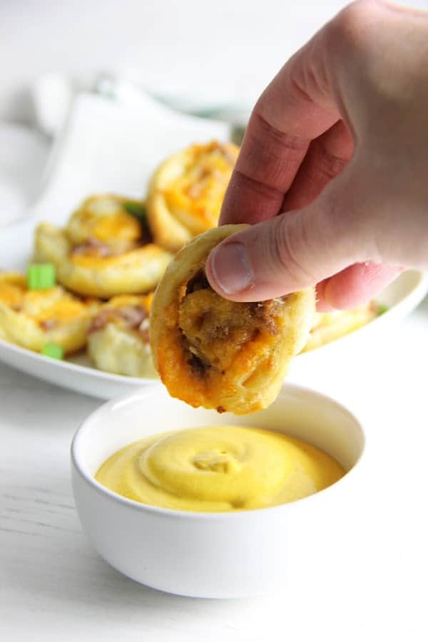 Puff Pastry Sausage Cheddar Pinwheels dipped into mustard