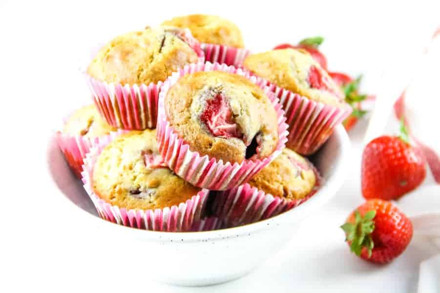 Strawberry Oatmeal Muffins in pink liners stacked in white bowl with fresh strawberries