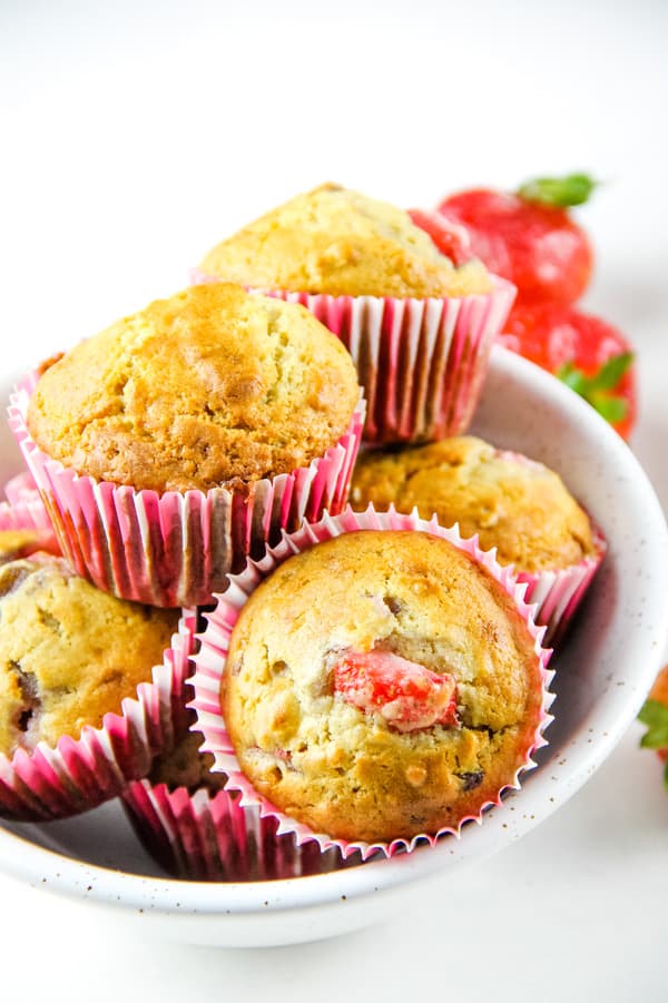 Strawberry Oatmeal Muffins stacked in white bowl with fresh strawberries