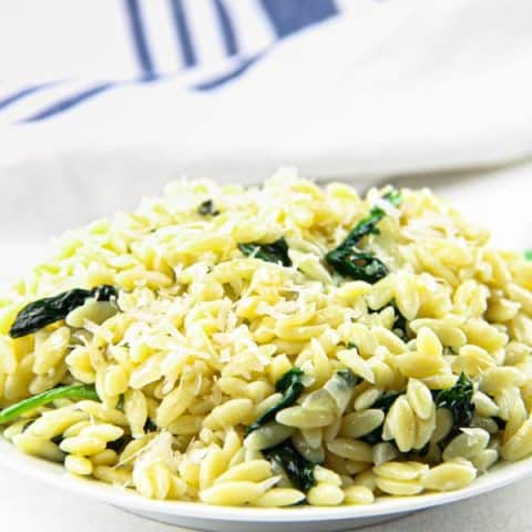 Cheesy Spinach Orzo on white plate with blue and white napkin in the background