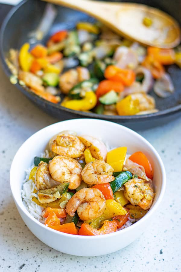 Garlic Thyme Shrimp and Veggies in white bowl with rice and sautee pan in background