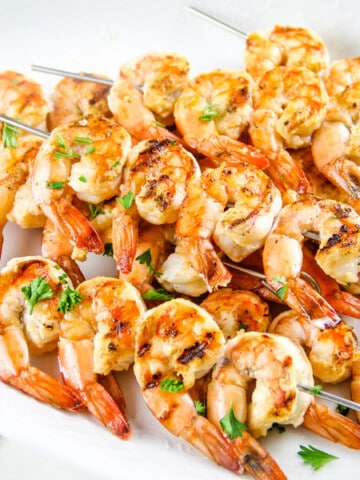 Grilled Lemon Shrimp Skewers on white plate with yellow towel topped with parsley