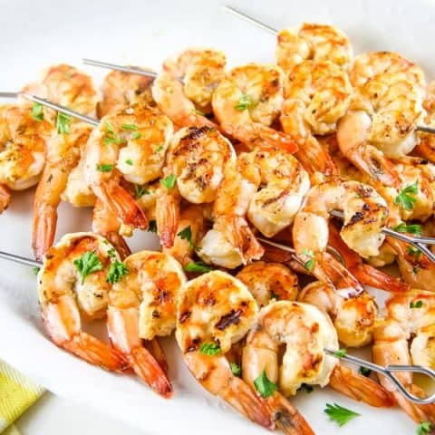 Grilled Lemon Shrimp Skewers on white plate with yellow towel topped with parsley