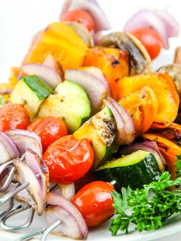 Grilled Vegetable Skewers on white plate with parsley and bowl of olive oil in background