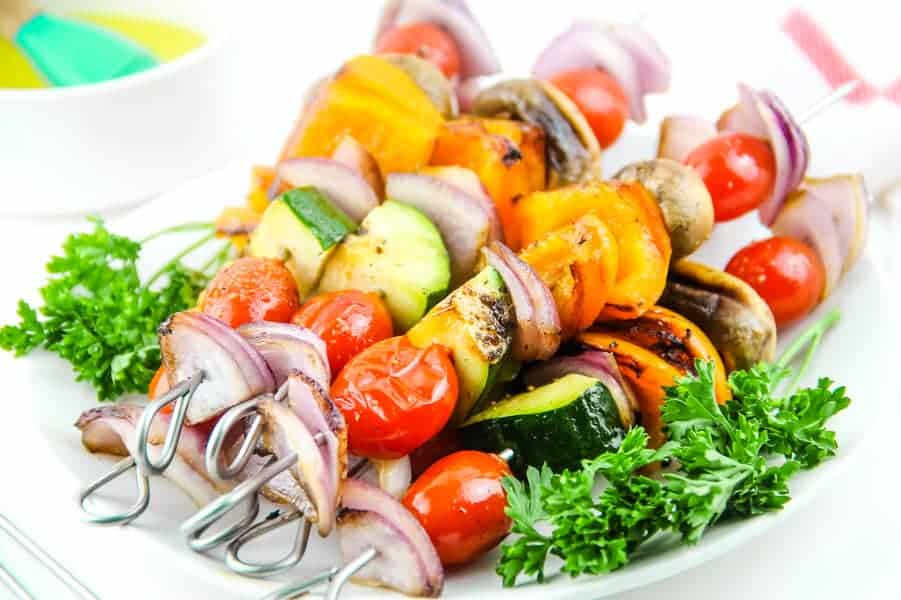 Grilled Vegetable Skewers on white plate with parsley and bowl of olive oil in background