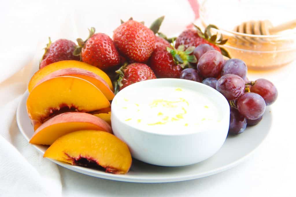 Honey Yogurt Dip in white bowl on grey plate with fresh fruit.