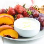 Honey Yogurt Dip in white bowl on grey plate with fresh fruit.