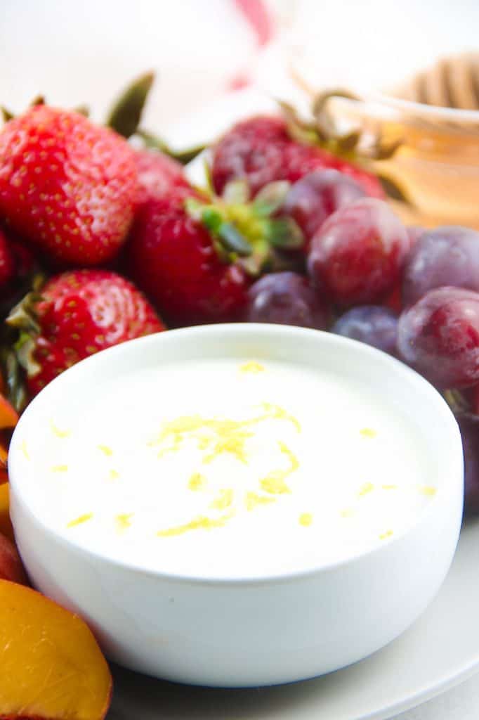 Honey Yogurt Dip in white bowl with fruit in background.