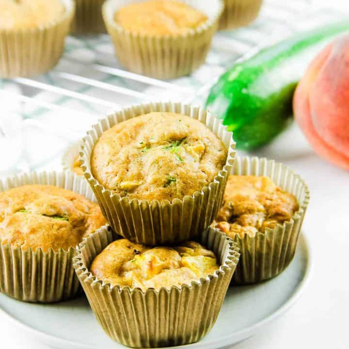 Peach Zucchini Oatmeal Muffins on white plate with zucchini and peach in background.