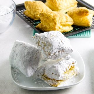 Air Fryer Beignets with tongs and bowl of powdered sugar.