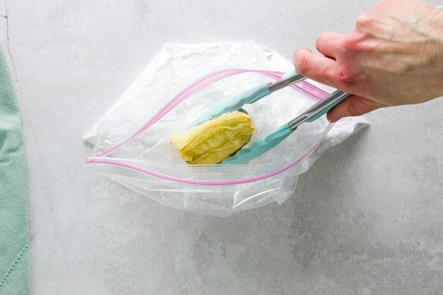 placing cooked beignet in plastic bag with powdered sugar.