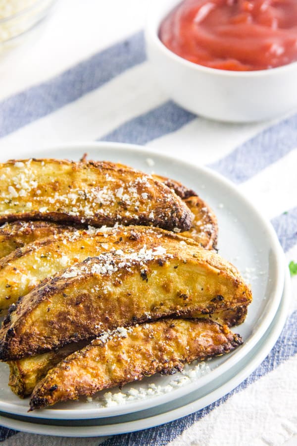 Air Fryer Parmesan Potato Wedges on white plate with extra cheese.