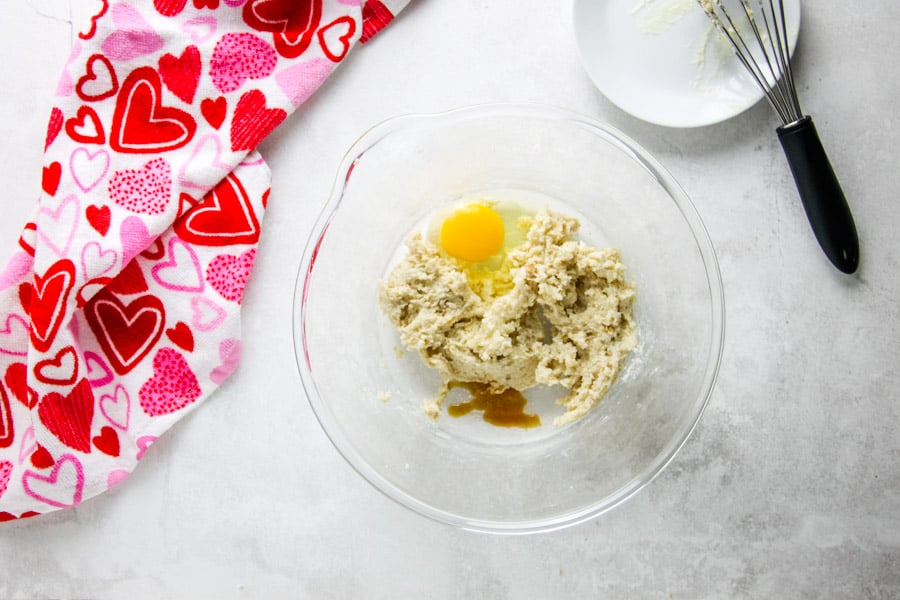 uncooked cookie ingredients in glass bowl with egg and vanilla