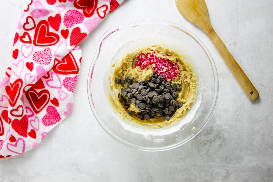 uncooked cookie ingredients in glass bowl with sprinkles and chocolate chips