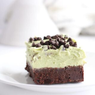 Mint Chocolate Chip Brownies slice on white plate with frosting on top.