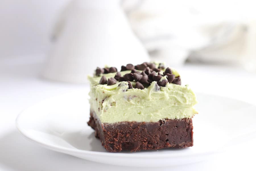 Mint Chocolate Chip Brownies slice on white plate with frosting on top.