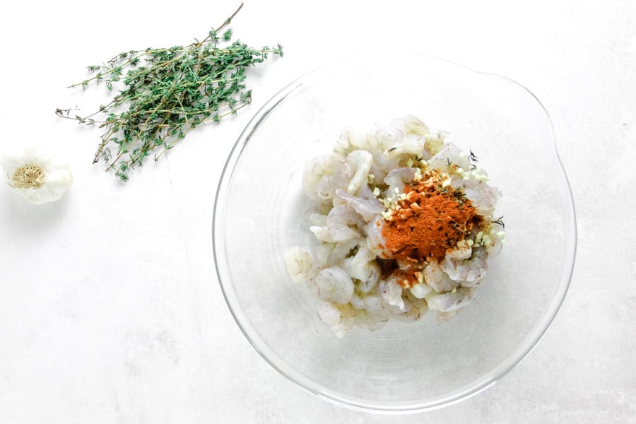 uncooked shrimp in glass bowl with seasonings.