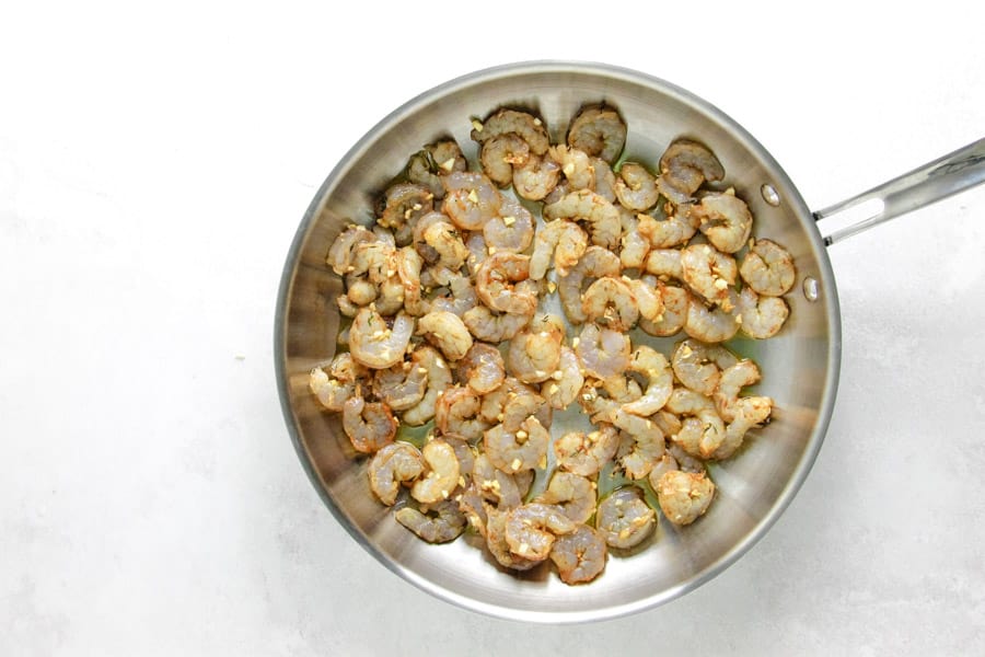 uncooked shrimp in glass bowl in pan with olive oil.