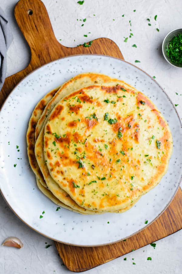 flatbread stacked on plate on wooden cutting board.