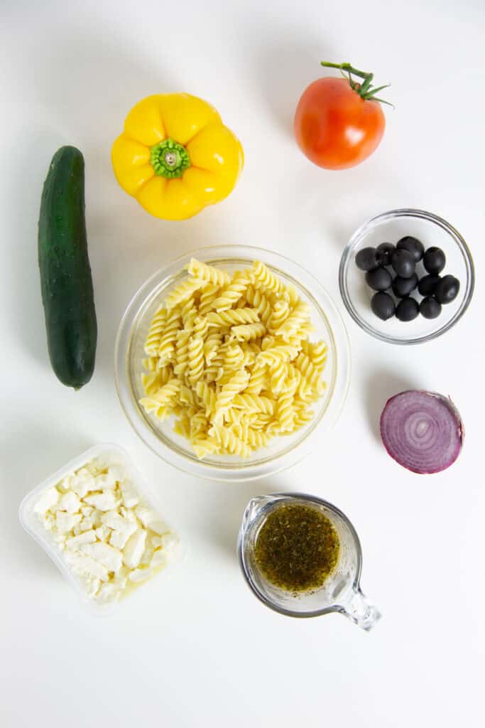 Greek Pasta Salad ingredients in glass bowls.