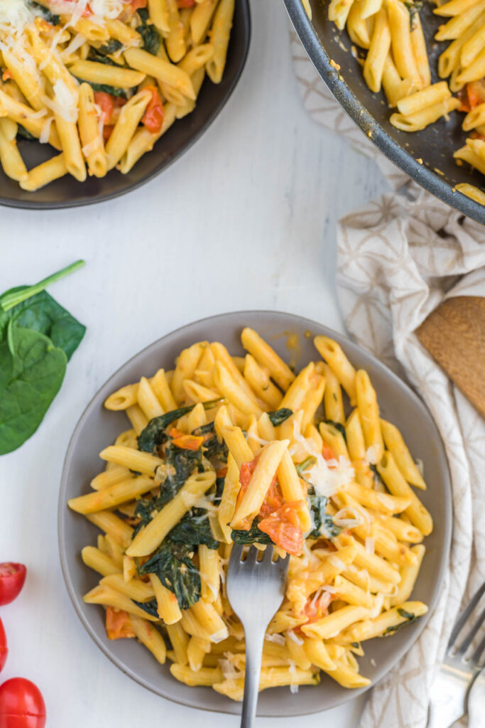 Creamy Tomato Spinach Pasta on gray plate with fork.