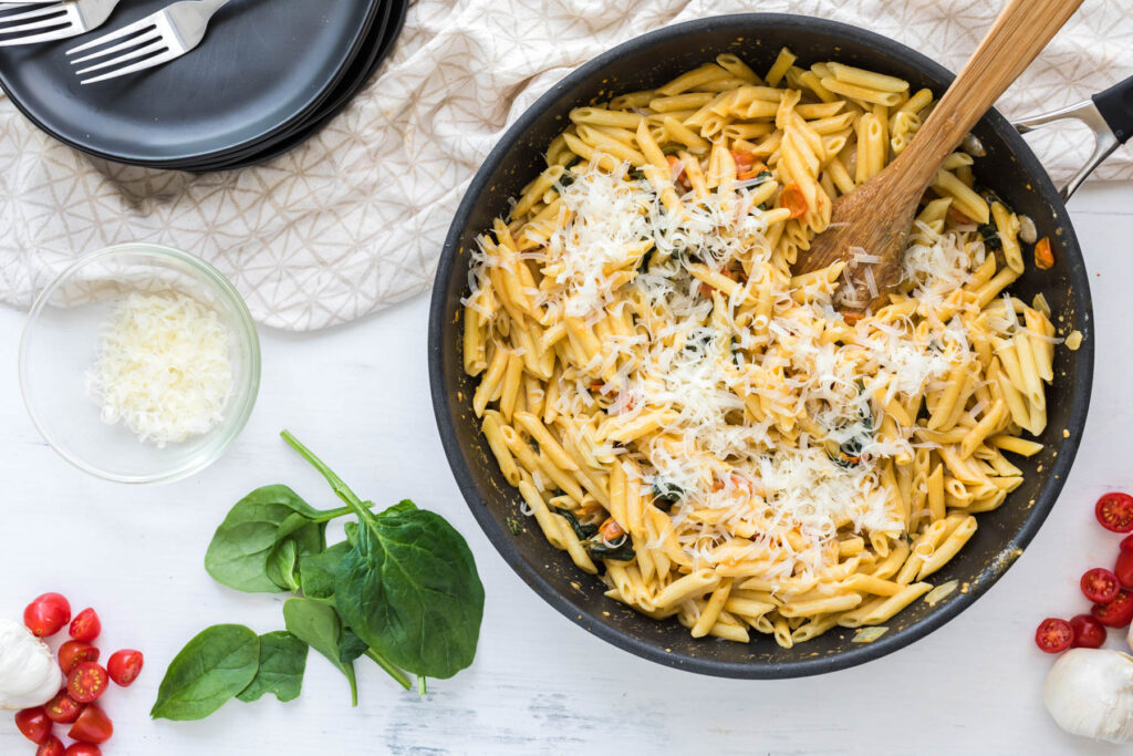 Creamy Tomato Spinach Pasta in pan topped with cheese.