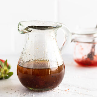 Strawberry Balsamic Vinaigrette in glass jar with strawberries in background.