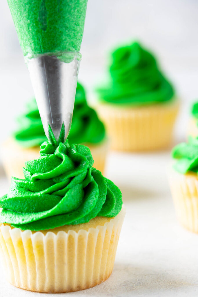 piping green frosting on top of vanilla cupcakes.