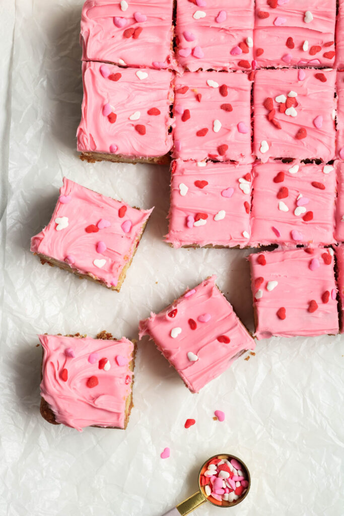 Strawberry Frosted Cookie Bars on parchment paper with sprinkles.