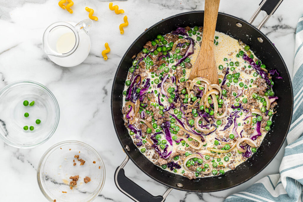 skillet with sausage, vegetables, and cream in skillet.