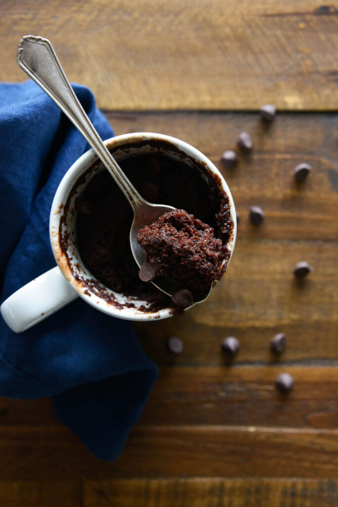 Easy Chocolate Mug Cake made in the microwave in under 2 minutes! Warm chocolate cake with easy ingredients and cooked to perfection! overhead view of Chocolate Mug Cake on brown background.