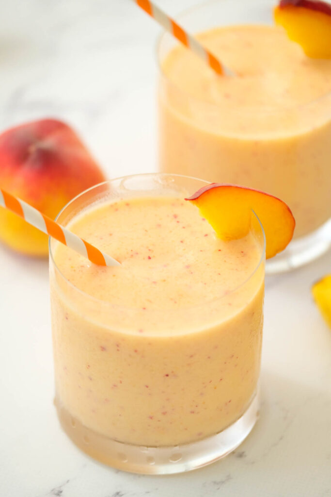 Peach Honey Yogurt Smoothie in glass with straw and peach slice.