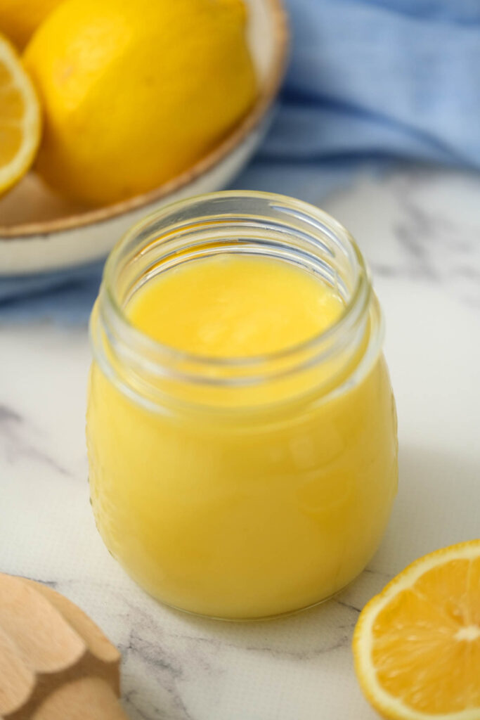 Homemade Lemon Curd in glass jar on white background.