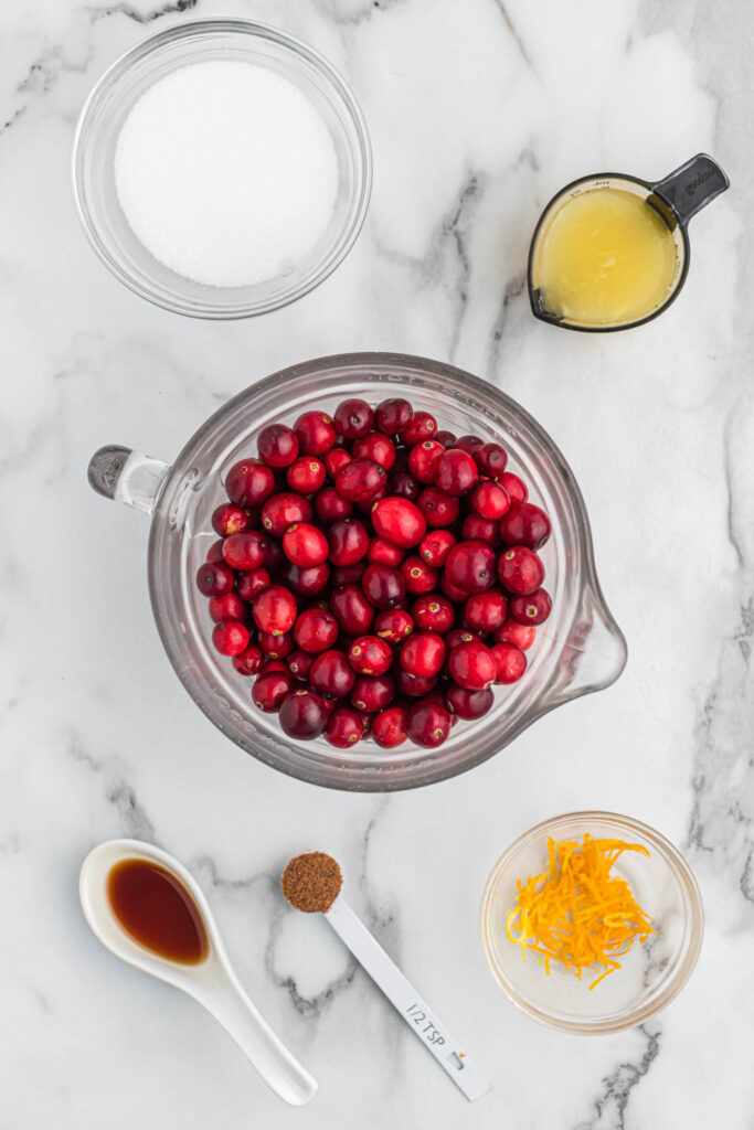 ingredients for orange cranberry sauce on white marble background.